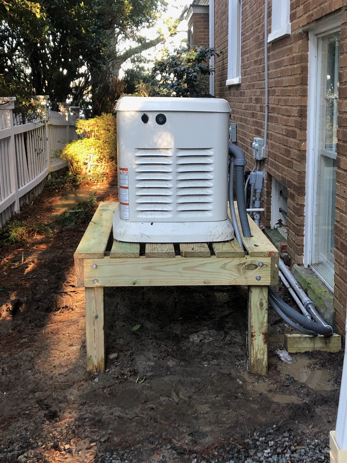 Generac air-cooled standby generator mounted on an elevated stand beside a brick home